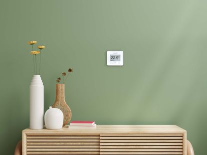 WundaSmart thermostat on a green wall with vases on a cabinet