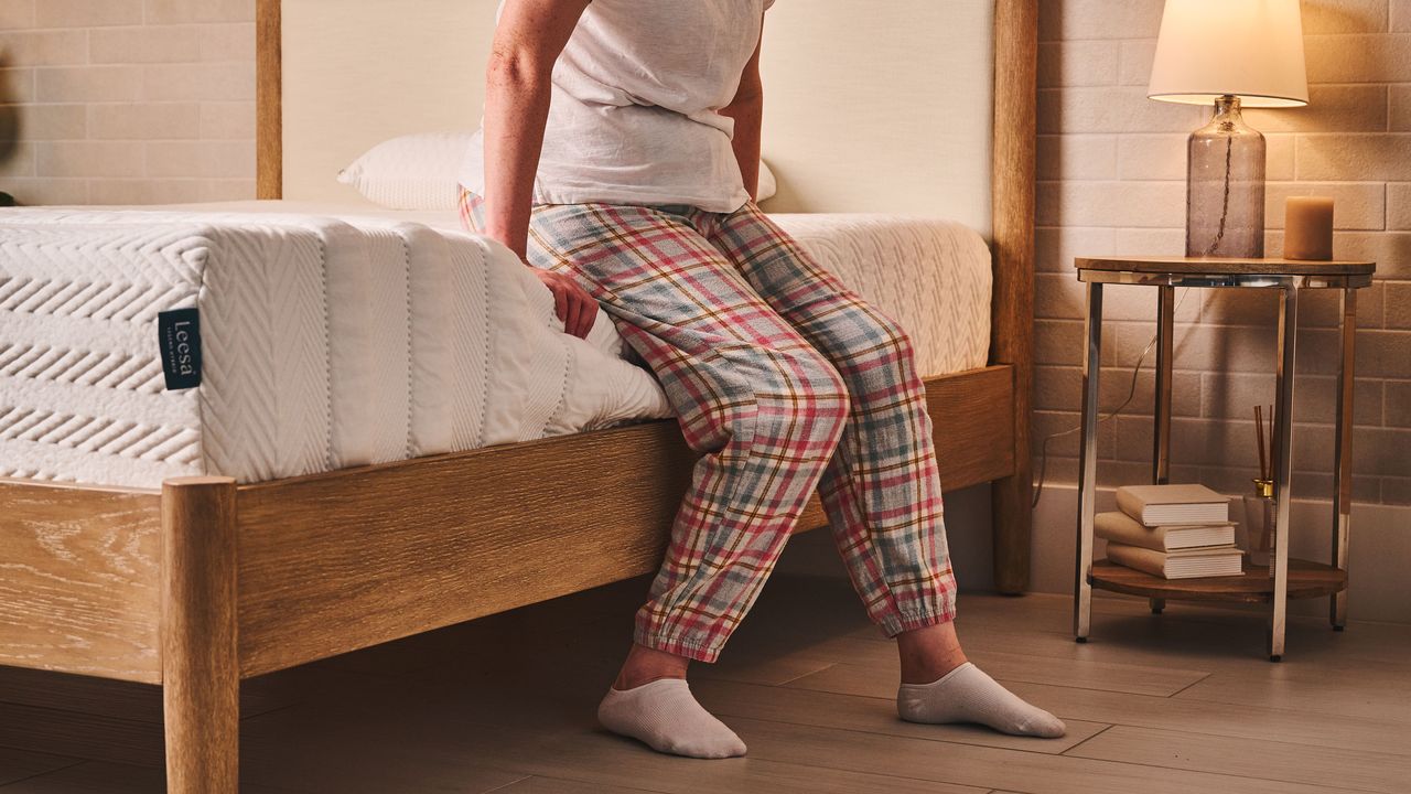 A person sits on the edge of the Leesa Legend Hybrid mattress, testing the edge support