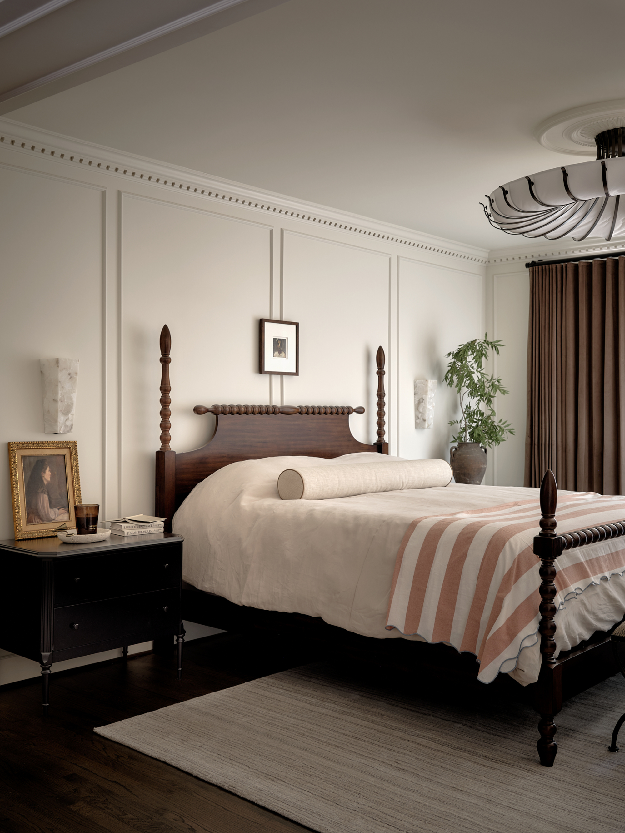 A bedroom with soft white walls, brown accents, and a bed with bobbin detailing
