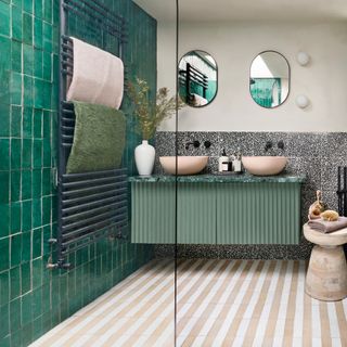 shower area with emerald green tiles, black hardware, a green fluted bathroom console unit with twin pink/beige basins, matching oval mirrors, two globe wall lights and black and white speckled splashback and black hardware