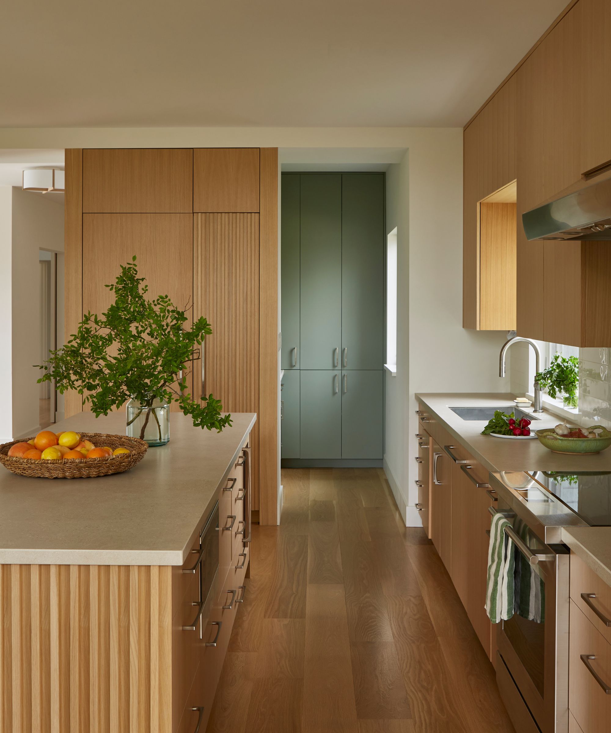 modern kitchen with wooden cabinets and floors, white walls, and green cabinets in adjoining pantry