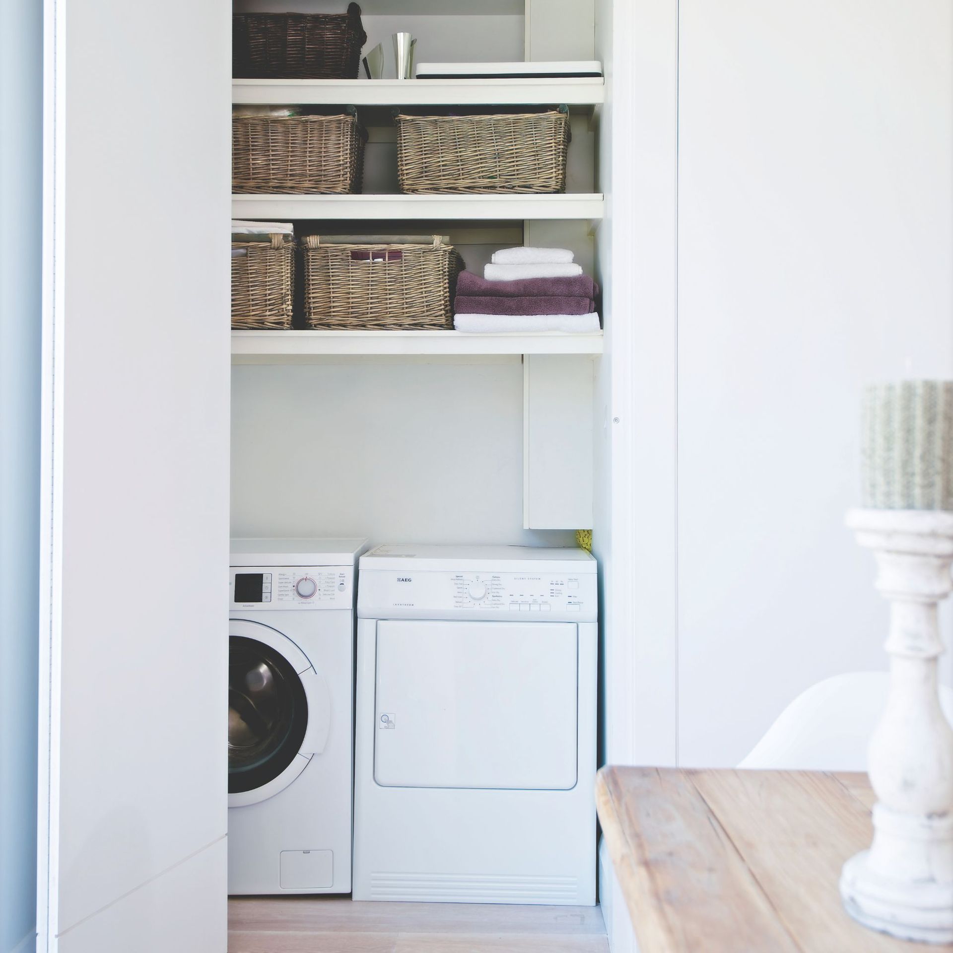 White utility cupboard with a washing machine and tumble dryer, and shelves with bedding and towels above them