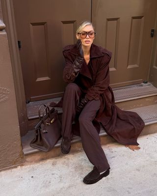 @hoskelsa wears a brown suede trench, with leather gloves, tailored trousers, loafers and a tote bag