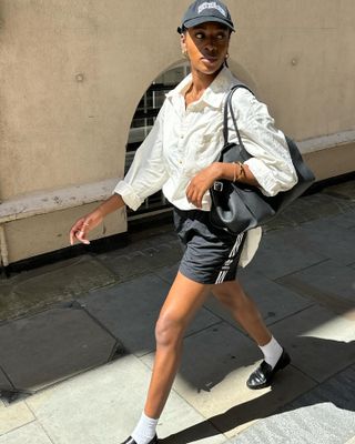 British influencer @georgia_3.0 wearing a white button-down shirt, Adidas track shorts, white socks with black loafers, and a black The Row Margaux Bag