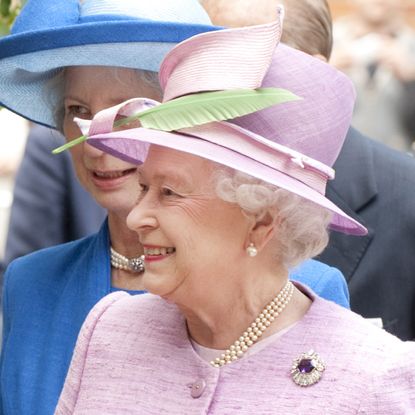 Queen Elizabeth wears a lilac coat and matching hat with a green feather and drops a bouquet given to her by a royal fan in 2010 at Eton