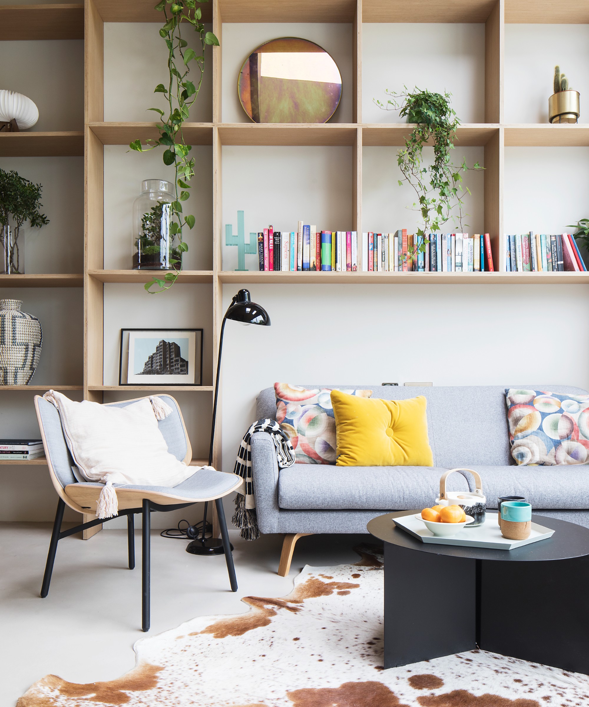 An open-plan living room with a shelving wall displaying personal items and a cow-print rug on the floor