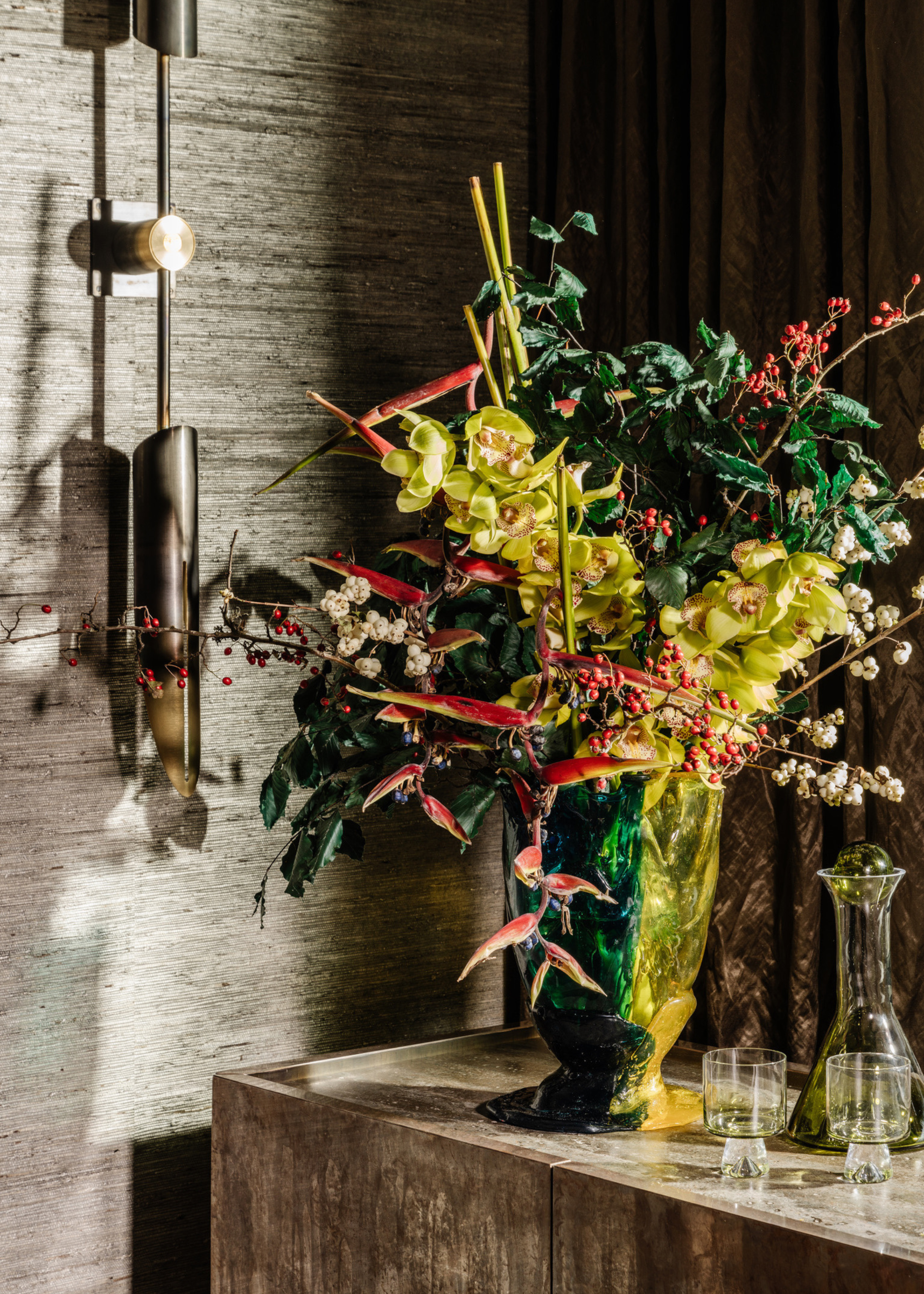 A vibrant floral display for Christmas on a counter next to a carafe and two wine goblets