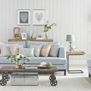blue and pink living room with vintage style coffee table on wheels, galvanised trunk, blue sofa, pink and blue cusihions, side table with lamp, heart artwork, sideboard with lantern, vases, cream rug