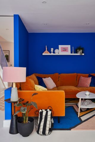 A blue living room paint color idea with orange velvet sofa furniture, a pink lampshade and black and white accessories