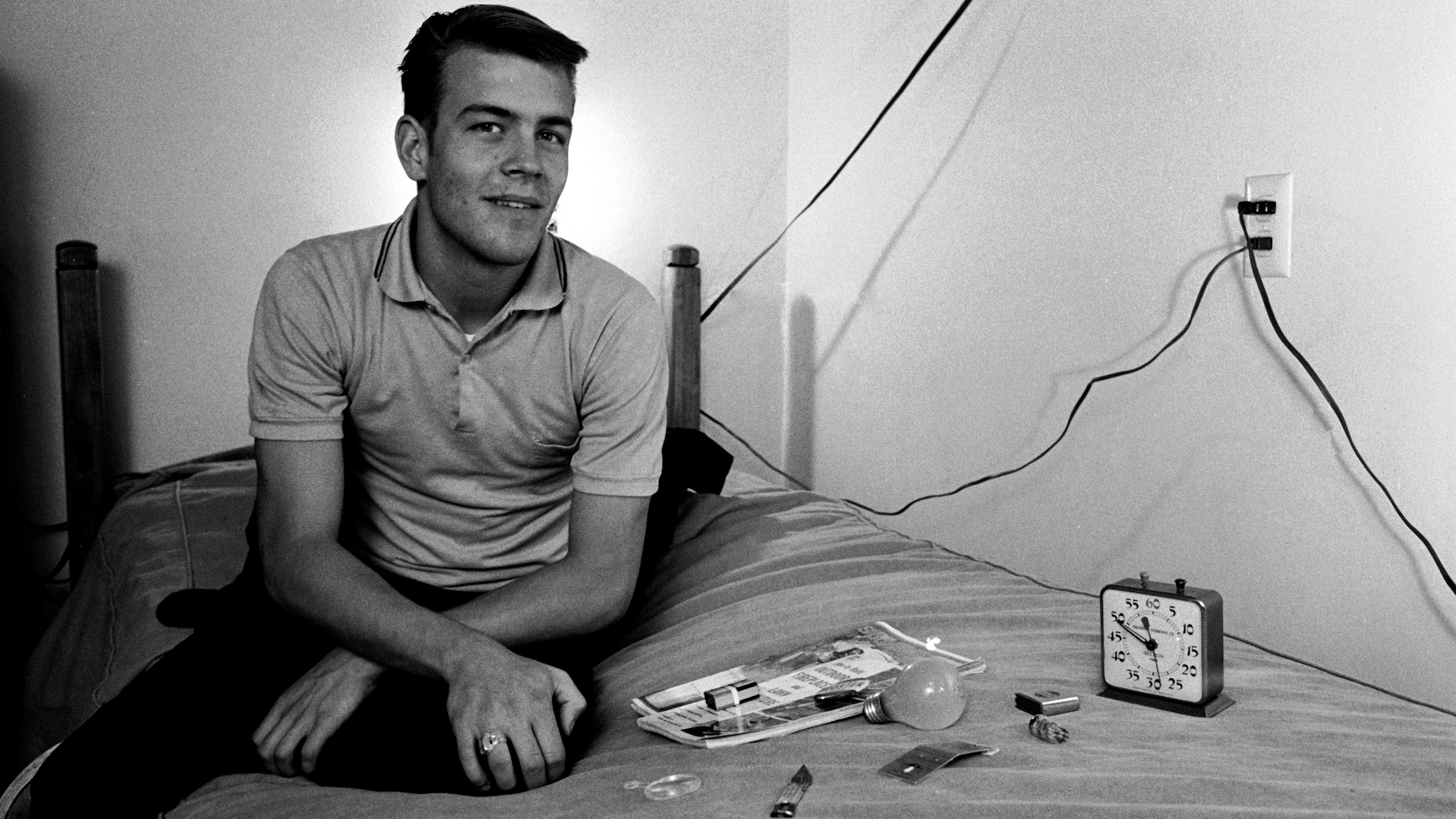 अमेरिकी छात्र रैंडी गार्डनर विभिन्न घरेलू वस्तुओं के बगल में एक बिस्तर पर बैठता है जिसे बाद में नींद की कमी के प्रयोग, सैन डिएगो, कैलिफोर्निया, 1964 के हिस्से के रूप में स्मृति द्वारा पहचानना होगा।