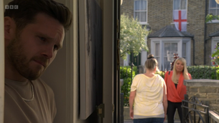 Karen Taylor blocks Sharon Watts outside her home. In the front of the picture, Keanu Taylor hides behind a wall and listens to their conversation outside.