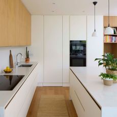 White kitchen with island, pendant lighting, wooden floor and built-in appliances
