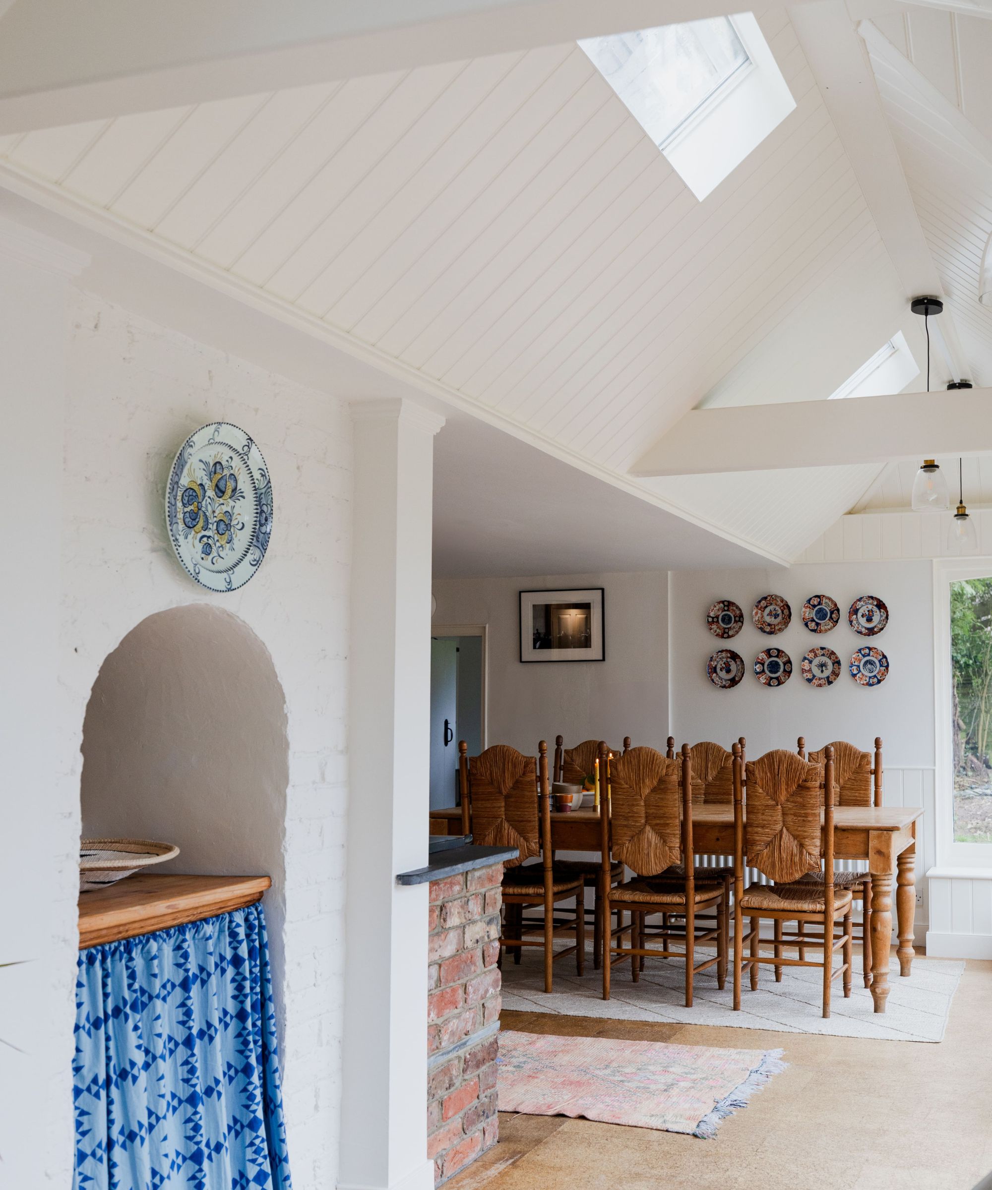 Open plan dining room with rattan chairs, a wooden dining table and plates hung on the wall