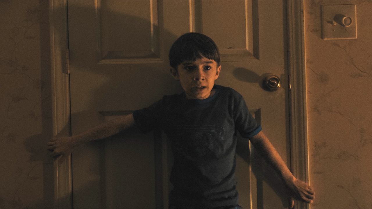 Alex looking horrified as he leans against a door in Weapons