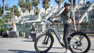 A woman sat stationary on her Ride1UP e-bike on a sunny street lined with palm trees