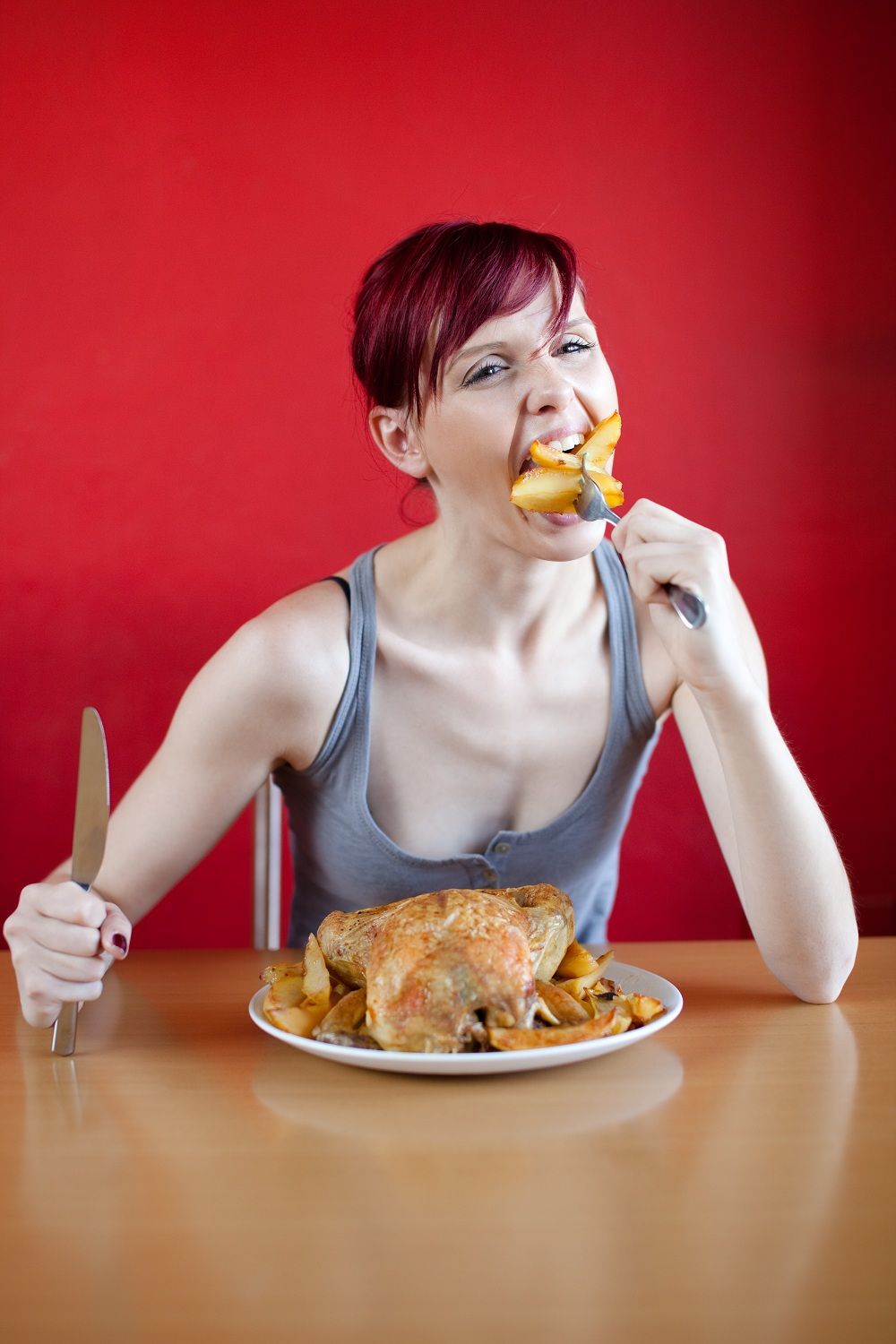 Skinny woman with a whole chicken on her plate stuffing herself with french fries.