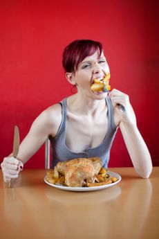 Skinny woman with a whole chicken on her plate stuffing herself with french fries.