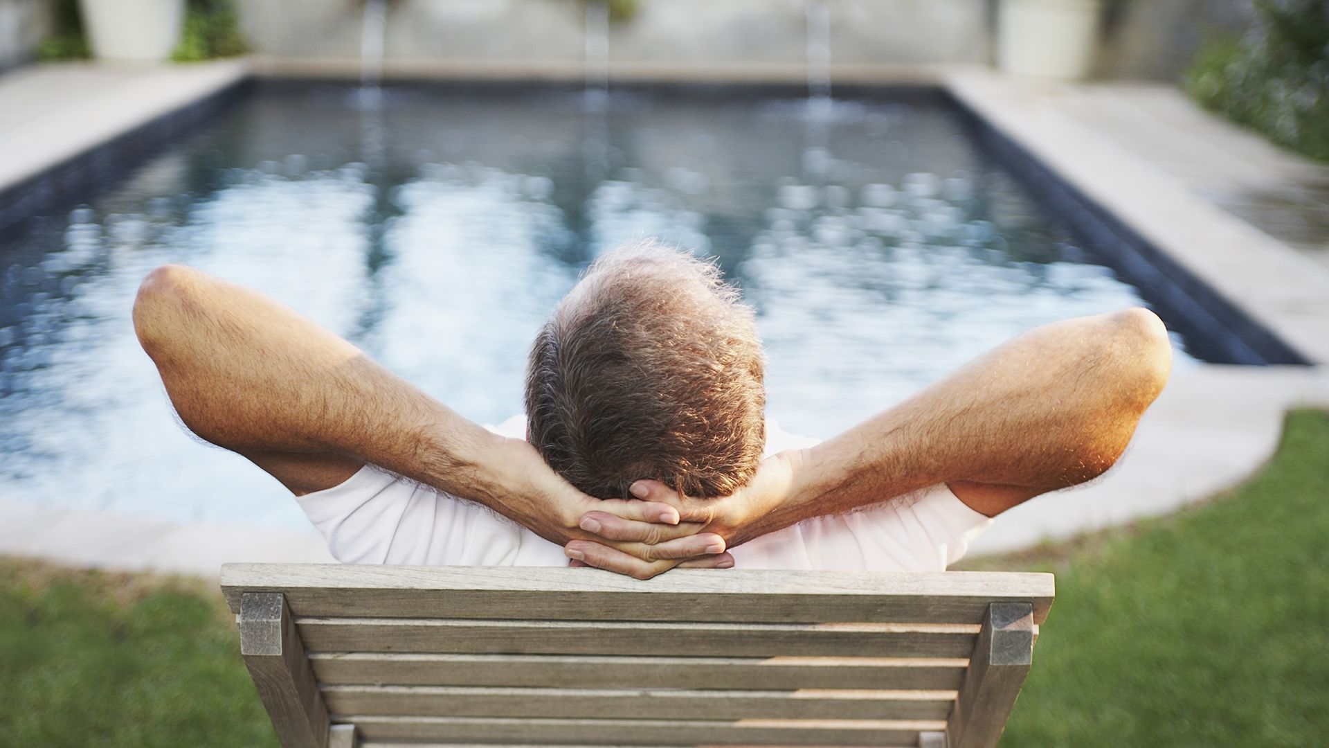 An older man relaxes as he faces a pool.
