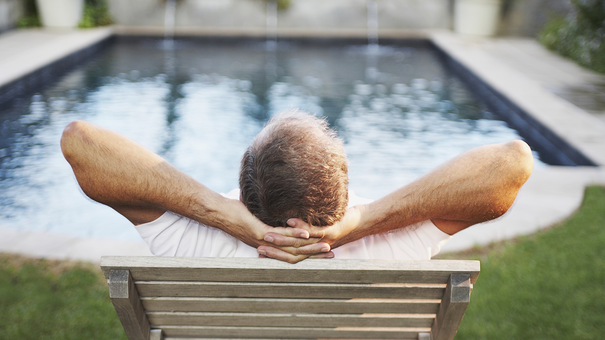 An older man relaxes as he faces a pool.