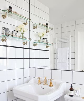An example of bathroom shelf ideas showing a white tiled bathroom with two wall-mounted glass shelves next to a white sink