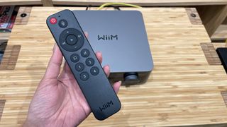 WiiM Ultra music streamer with remote control held in hand above it