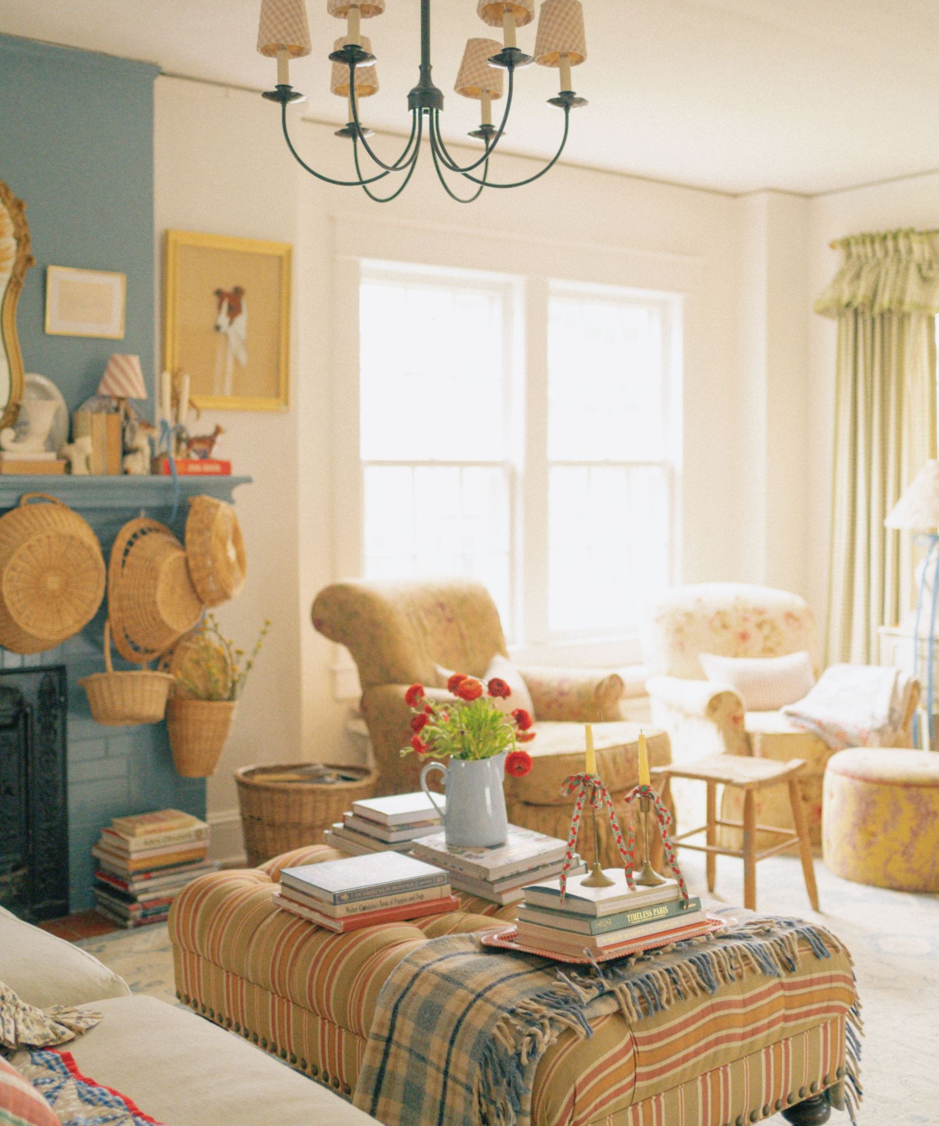 Eclectic living room with upholstered ottoman carrying books and vase, fireplace hung with baskets and armchairs