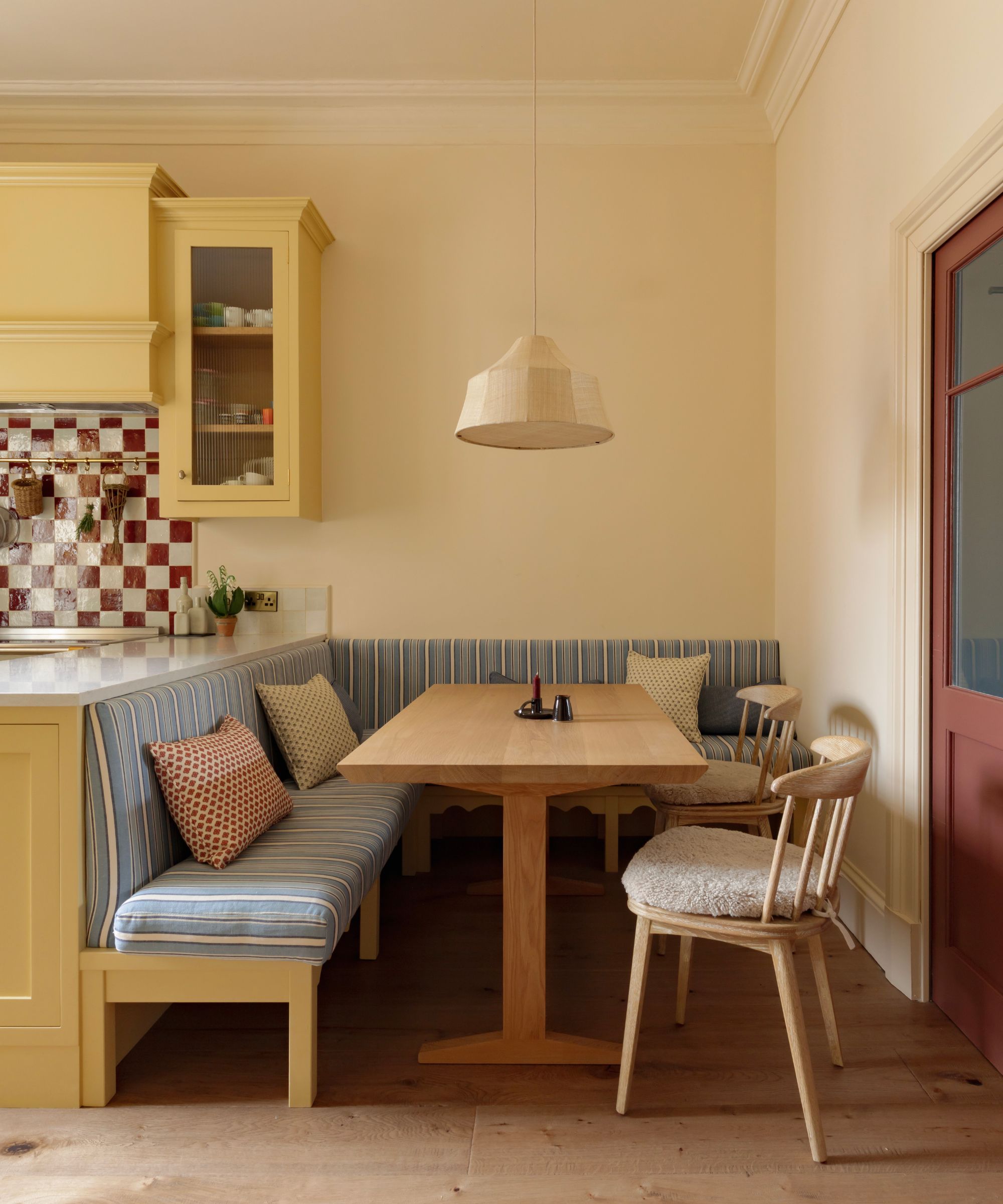 Built-in banquette seating in a Georgian kitchen with blue striped upholstery, wooden dining table, shearling dining chairs, and yellow Shaker cabinetry.