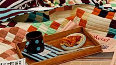 Wood breakfast tray with blue and burgundy patterned notebook and mug, on colorful patchwork quilts