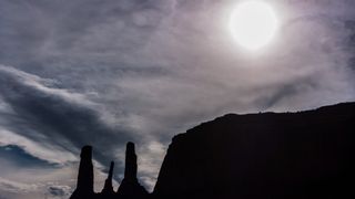 the sun can be seen in the sky above three tall spires of rock in the desert