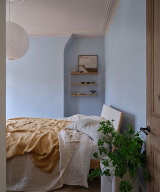 bedroom with light blue walls, neutral bedding and houseplant in corner