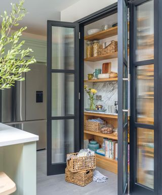 Large kitchen larder with sleek black metal doors with fluted glass panels, woven storage baskets