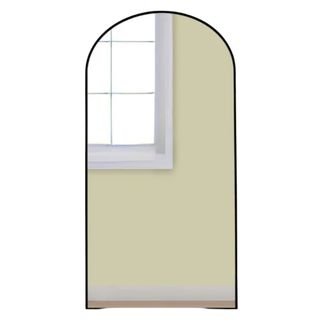 A black arched mirror reflecting a window and yellow wall