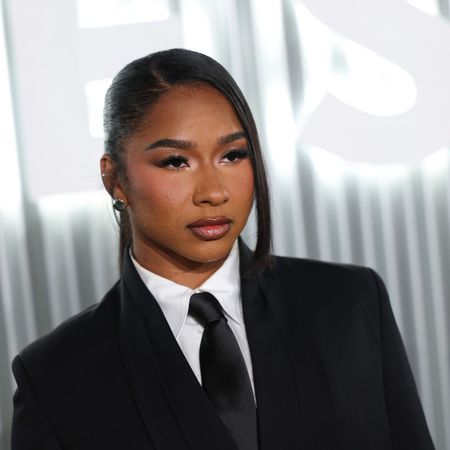 a black woman with dark hair wears a black suit in front of a white background