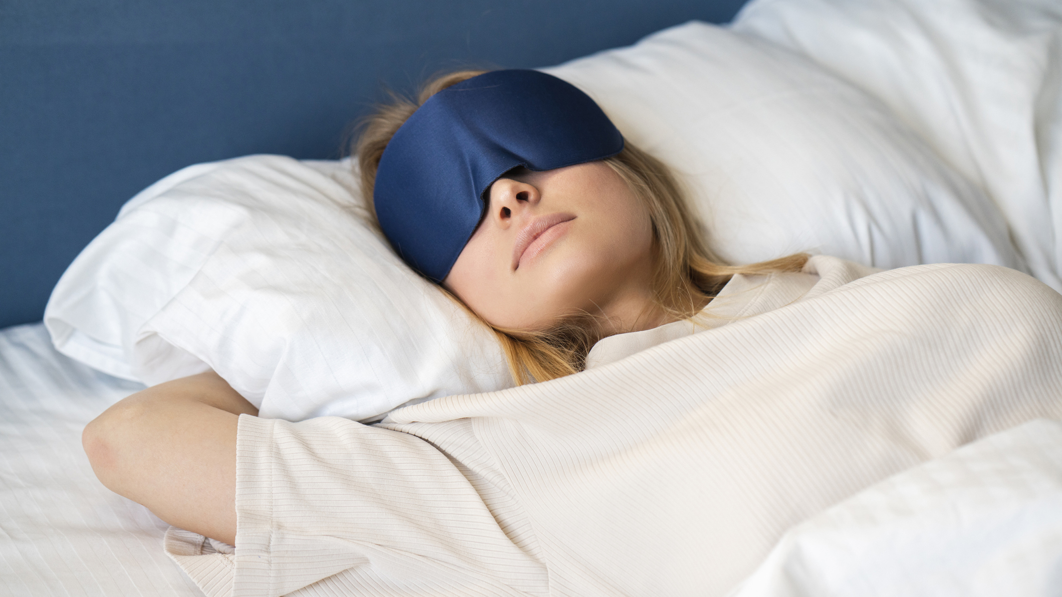 Uma mulher com cabelo loiro usando uma máscara de olhos azuis dorme em um sofá-cama