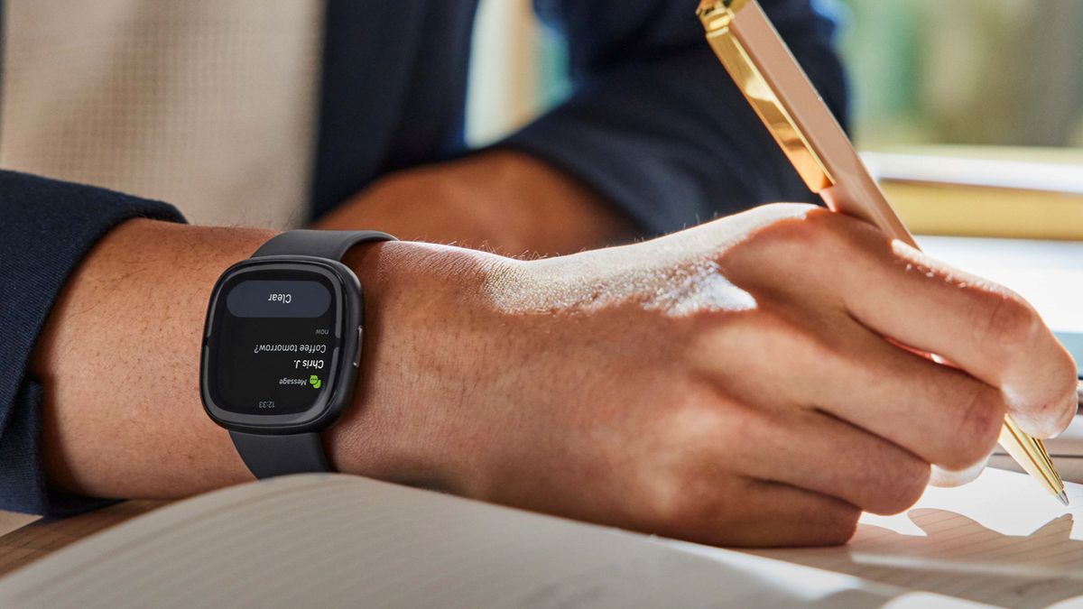 Fitbit Sense 2 on a person&#039;s wrist as they write in a notebook