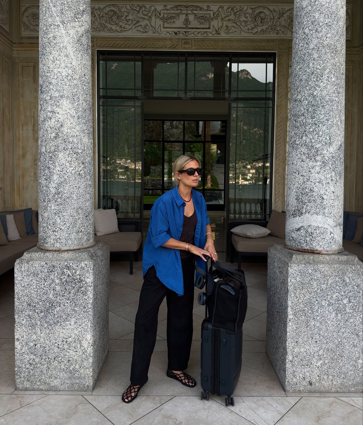 Influencer @Lucywiliums wears black trousers with 02 black mesh ballet flats and cobalt blue shirt. He had a suitcase in his hands and a red bead wears necklaces.