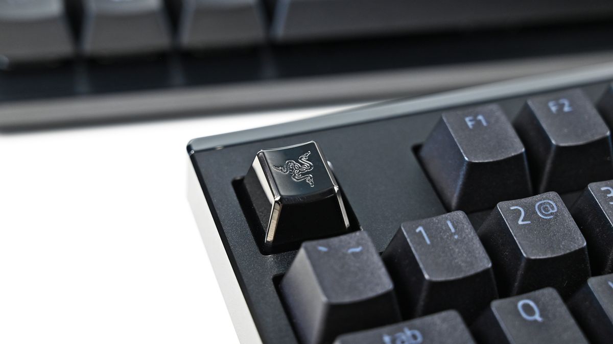 Extreme close-up of a glossy, metallic black custom keycap featuring the Razer triple-headed snake logo on a mechanical keyboard.