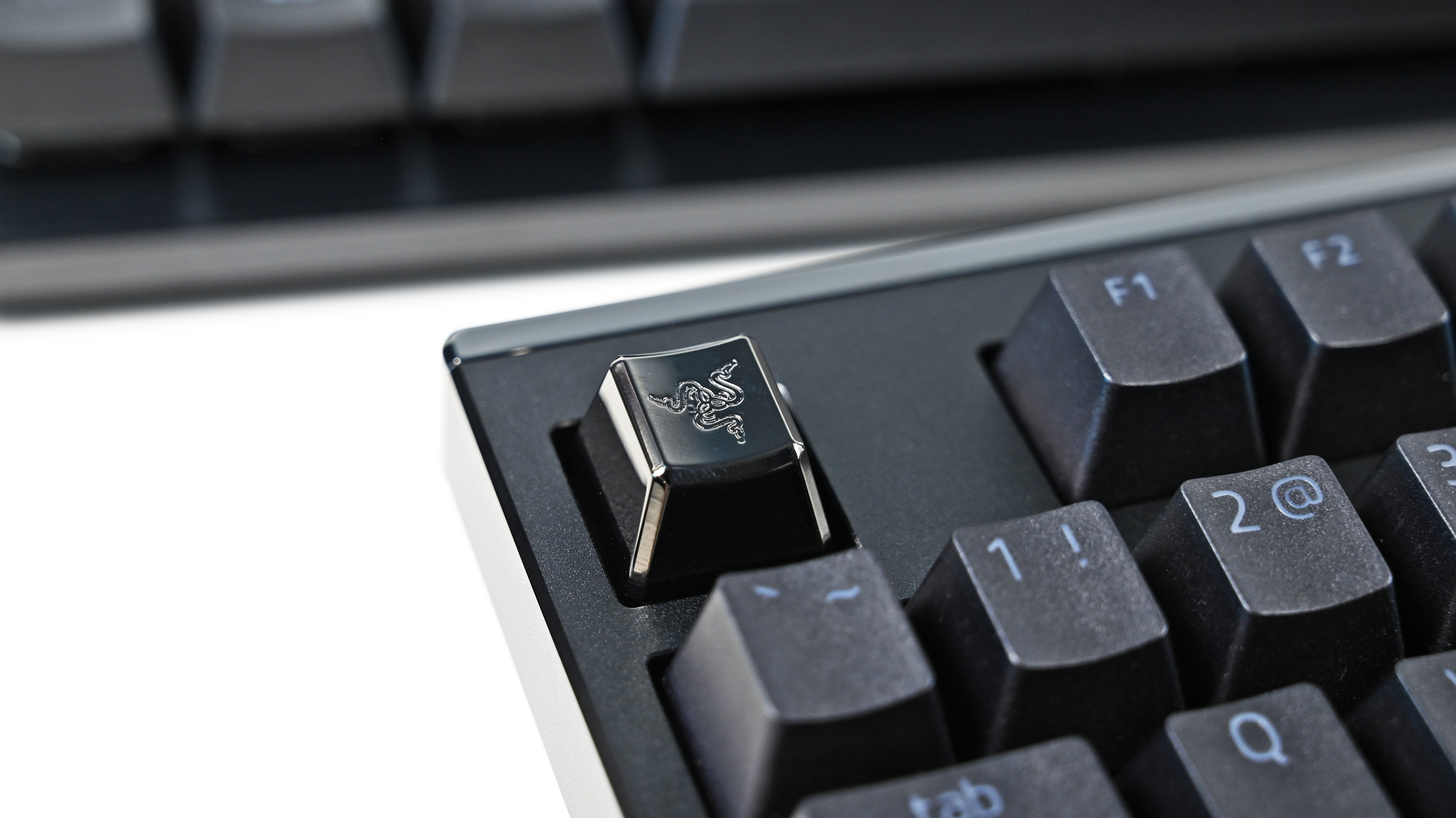 Extreme close-up of a glossy, metallic black custom keycap featuring the Razer triple-headed snake logo on a mechanical keyboard.
