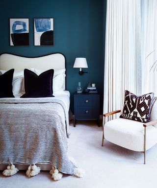 A blue bedroom with white curtains and carpet, with white and dark blue headboard and bedding
