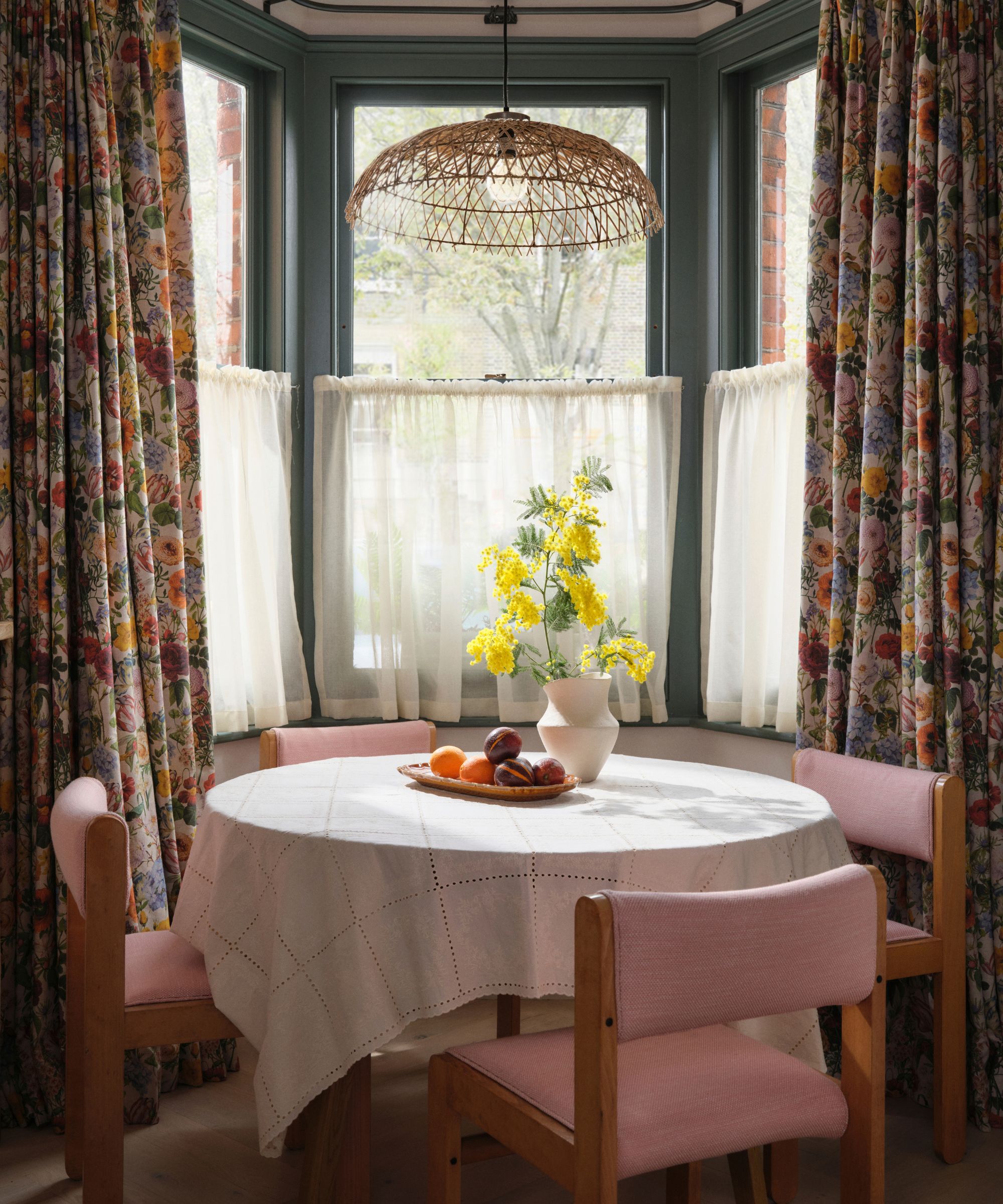 A dining nook with floral curtains and pink chairs