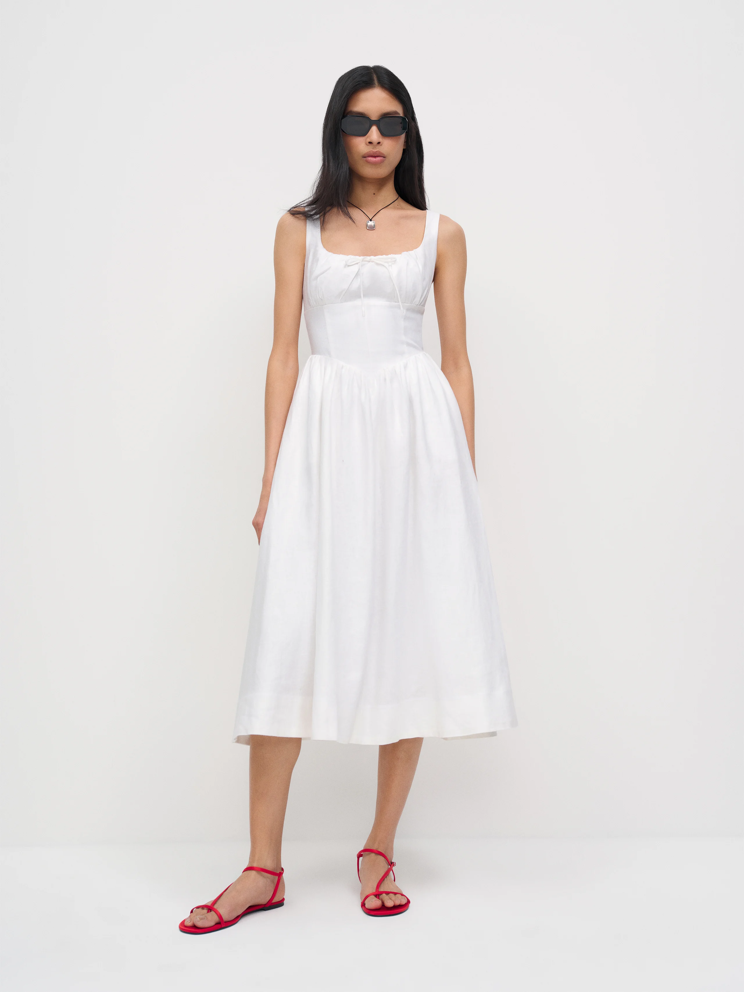 Model wears white dress and red sandals