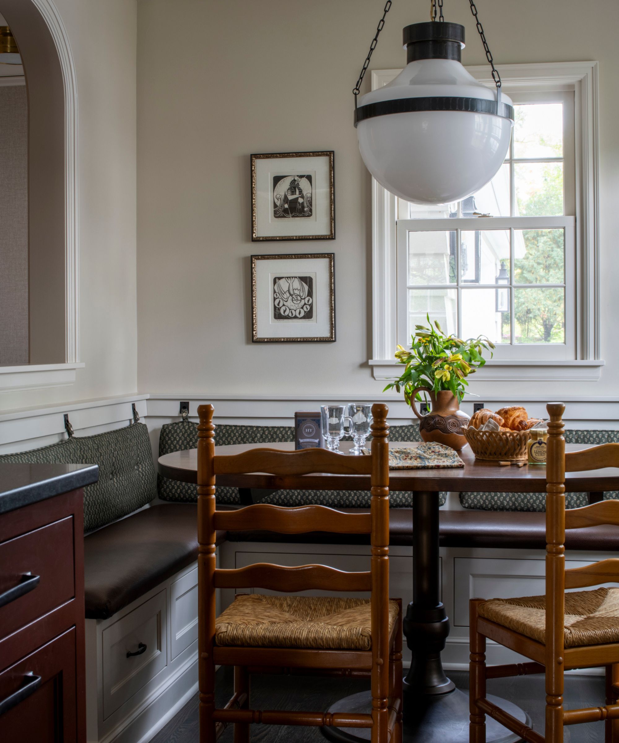 breakfast nook with a banquette upholstered seat, wooden table and pine antique chairs with a vintage white and black light overhead