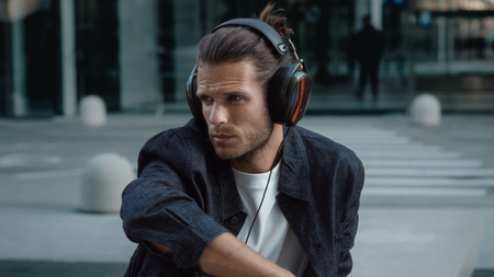 A man sitting outside a modern-looking building wearing the Meze Audio Strada headphones