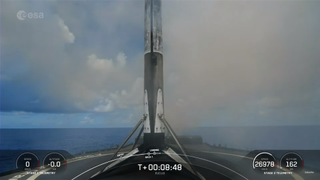 A soot-covered SpaceX white and black rocket standing on top of a landing platform in the ocean