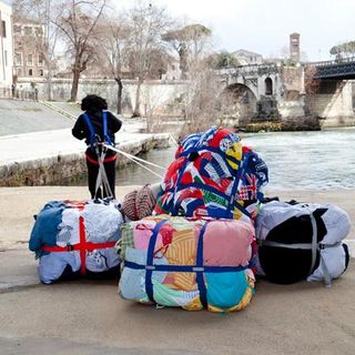 A person tugs bales of used clothing along the banks of the Tiber River. It's one of the characters from the exhibition.