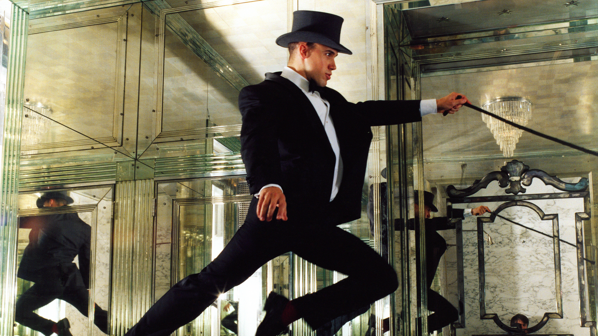 Miles Redd wearing a top hat and black suit jumping in the air in the middle of a mirrored room
