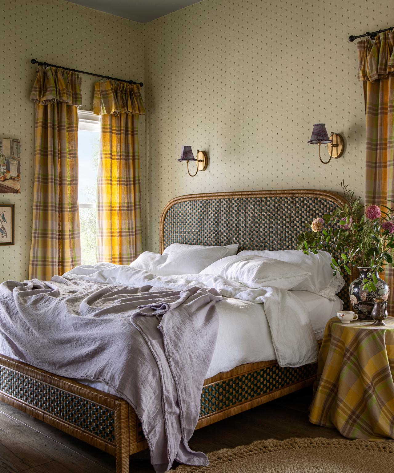 a cozy bedroom with tiny floral motifs on the wallpaper, a woven bedframe, and plaid printed drapes in yellow and brown