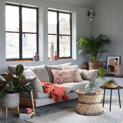 living room colour schemes, grey living room with tongue and groove walls, cream sofa, rattan side table, baskets, artwork, plants, textured cushions, rug, vases 