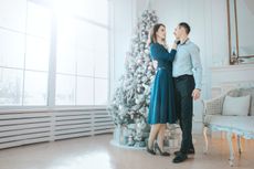 A man and a woman embrace in front of a Christmas tree. 