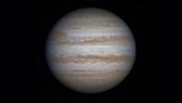 Photo of Jupiter as seen through a telescope. A large white sphere with swirling rings of red and brown around it against a black background.